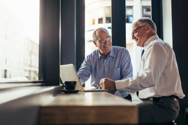 Two senior business men working together in modern cafe. Business partners sitting near window with laptop on table at restaurant.